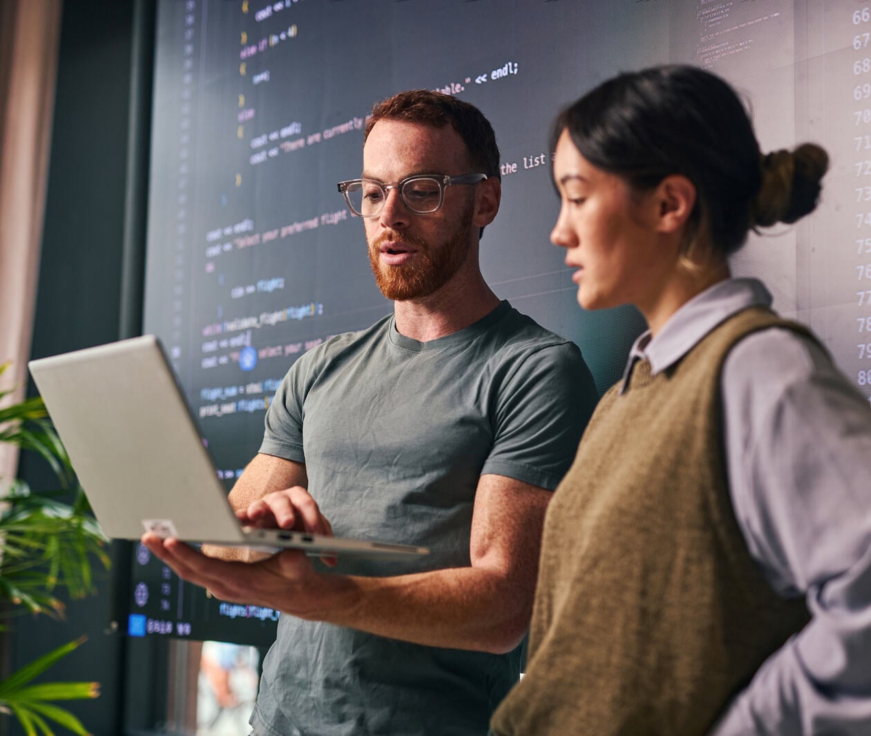 Two people working together standing while one holds the computer and works