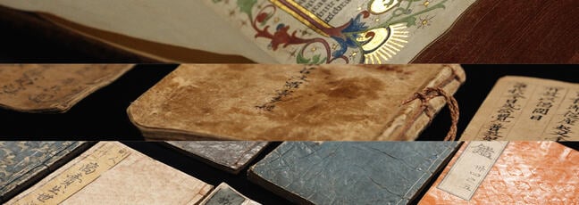 Rare and old First edition books are lined up along a bookshelf. They are leather bound and in poor condition.