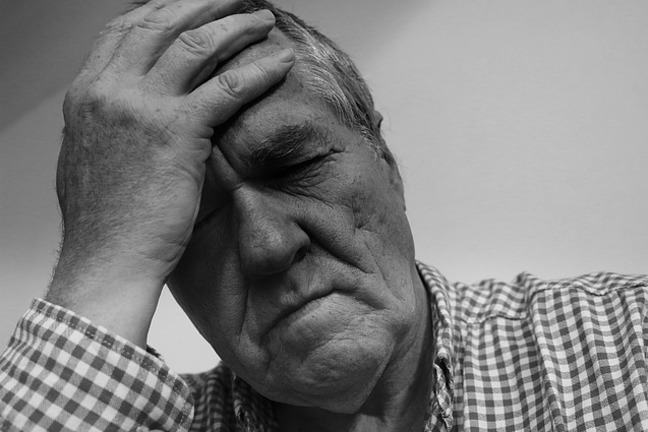 Black and white image of an older gentleman resting head on right hand, eyes closed and appears in discomfort