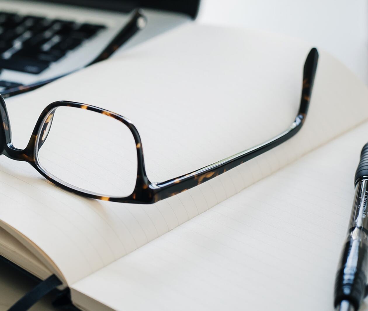 A pair of glasses and a pen on a notepad. 