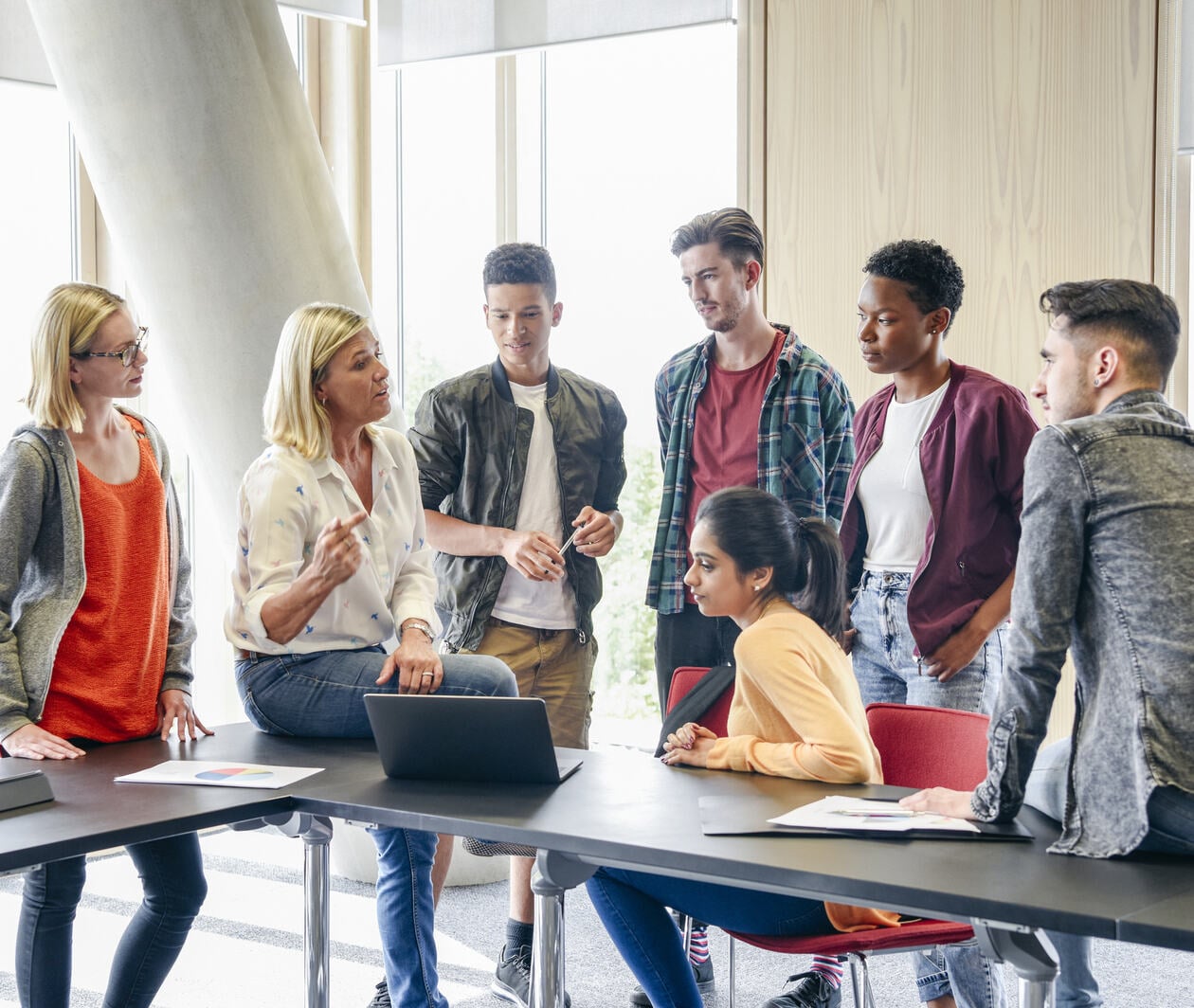 Six college students listening to mature female lecturer with laptop in classroom