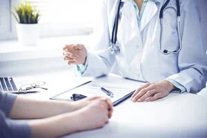 Doctor and female patient sitting at the desk and talking in clinic near window. Medicine and health care concept. Green is main color A