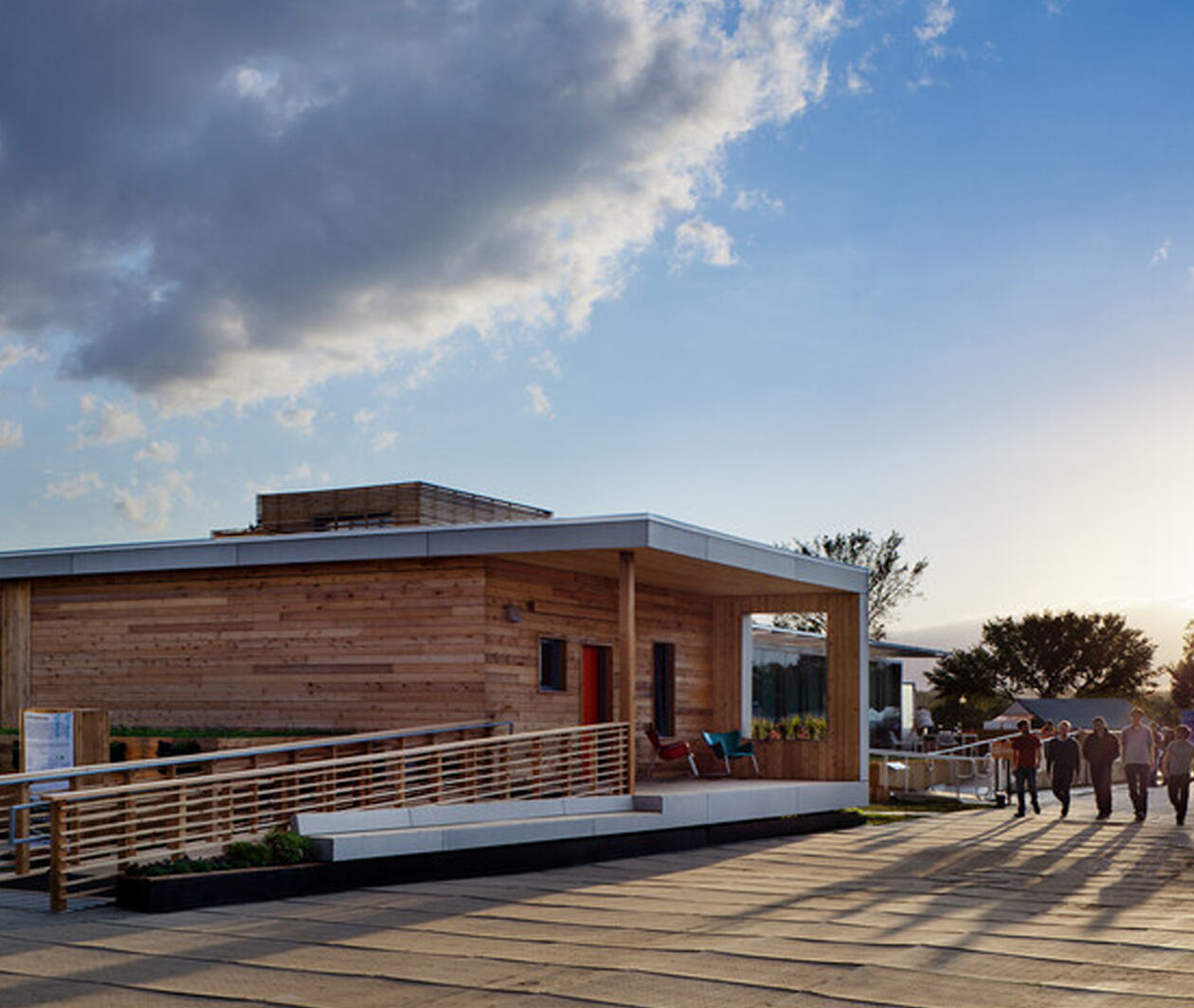 A building with sustainable wood and building materials with 5 people waking along the side with sunset at the background.