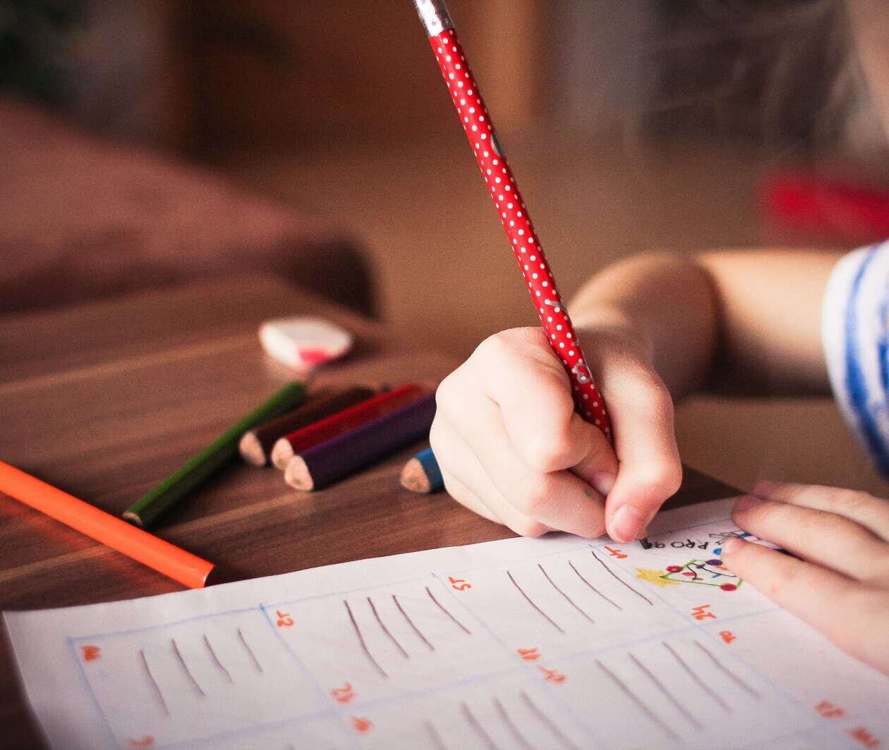 Autistic young student drawing on a worksheet with a few coloured pencils in an inclusive classroom.