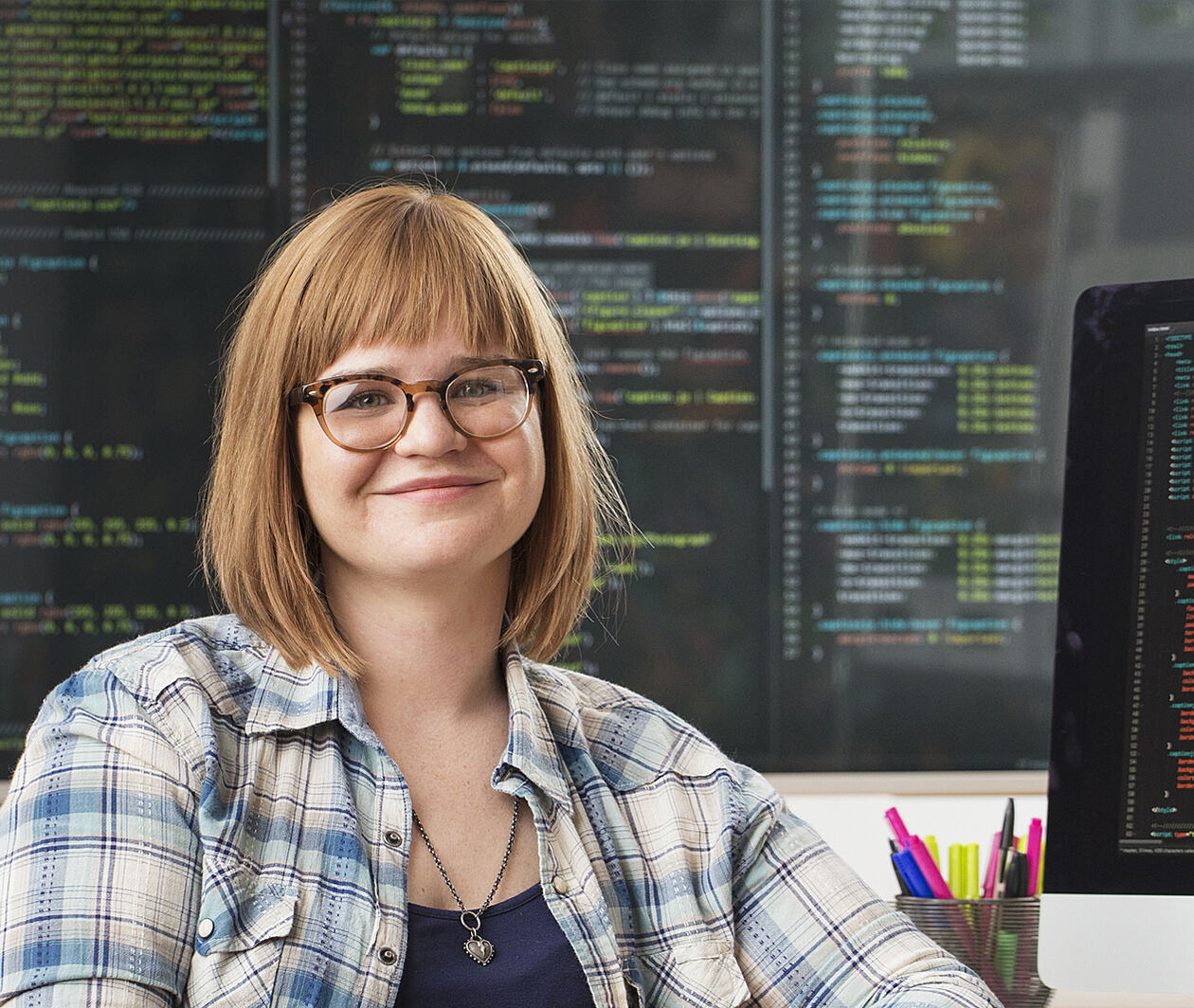 Woman smiling in front of screens showing lines of code