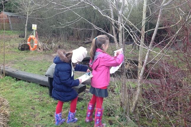 A photo of 2 children standing outside by a tree recording their measurements on a tally sheet