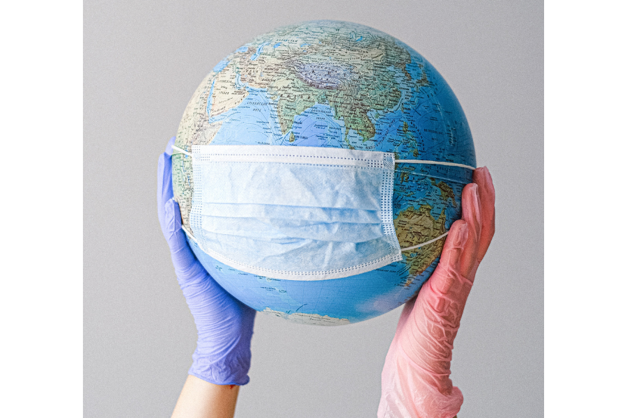 Globe held up by gloved hands, wearing a face mask