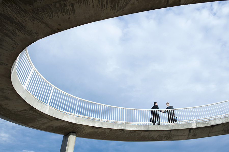 Caucasian businessmen shaking hands on elevated walkway.