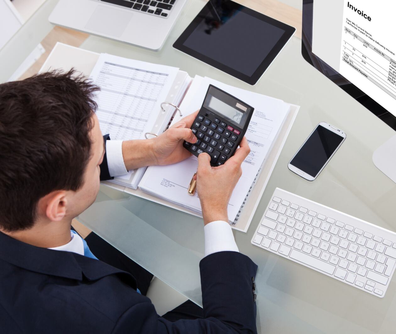 A business man holding a calculator working on the annual information statement on a computer.