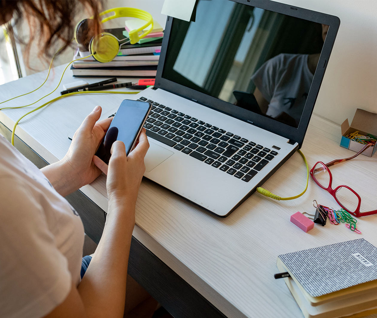 A learner learning at home, in front of a laptop and holding a mobile phone