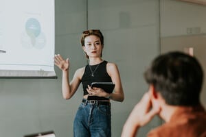 Four multinational students in front of a college building holding books, a laptop and pens.