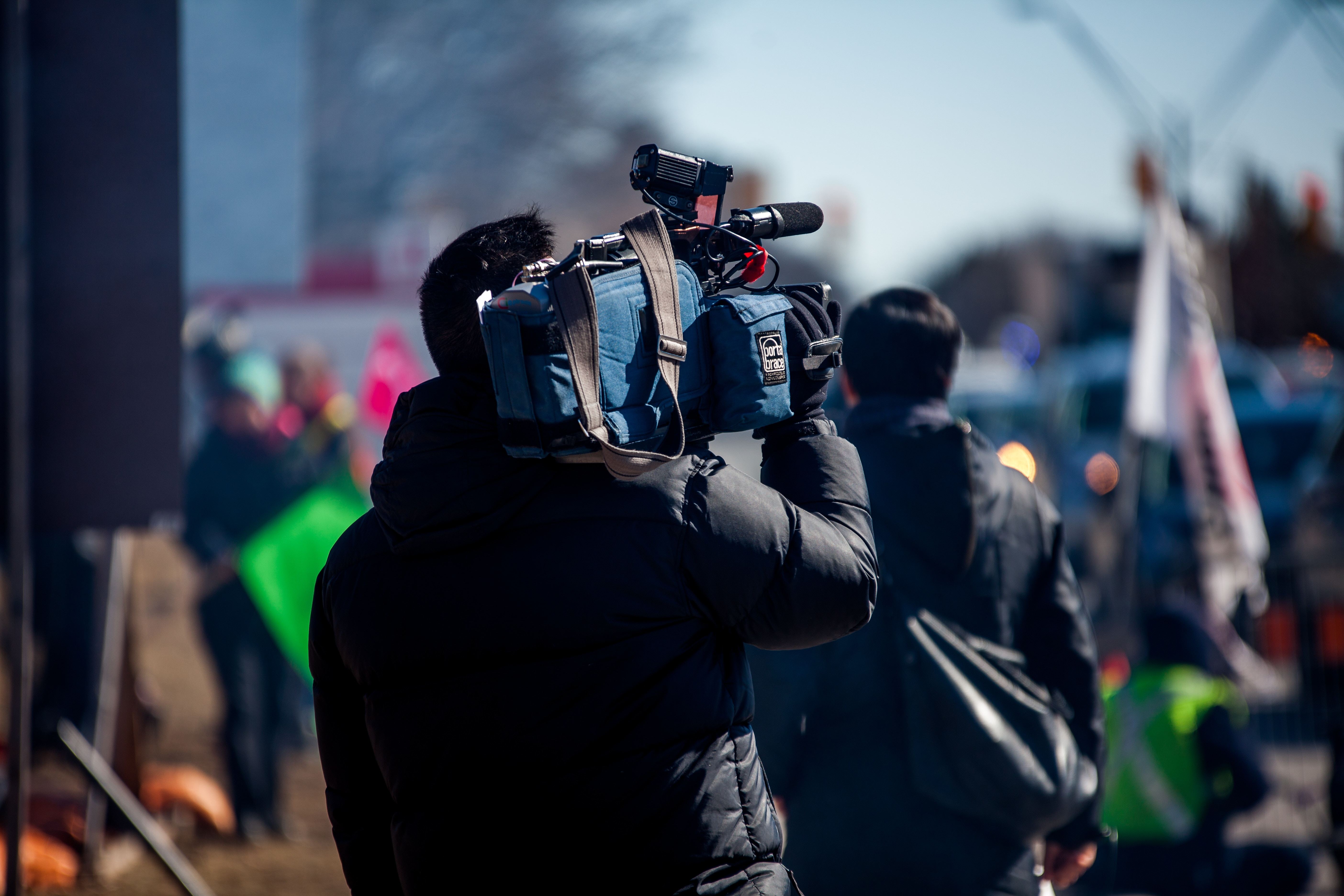 A camera crew shoulder their equipment through the street