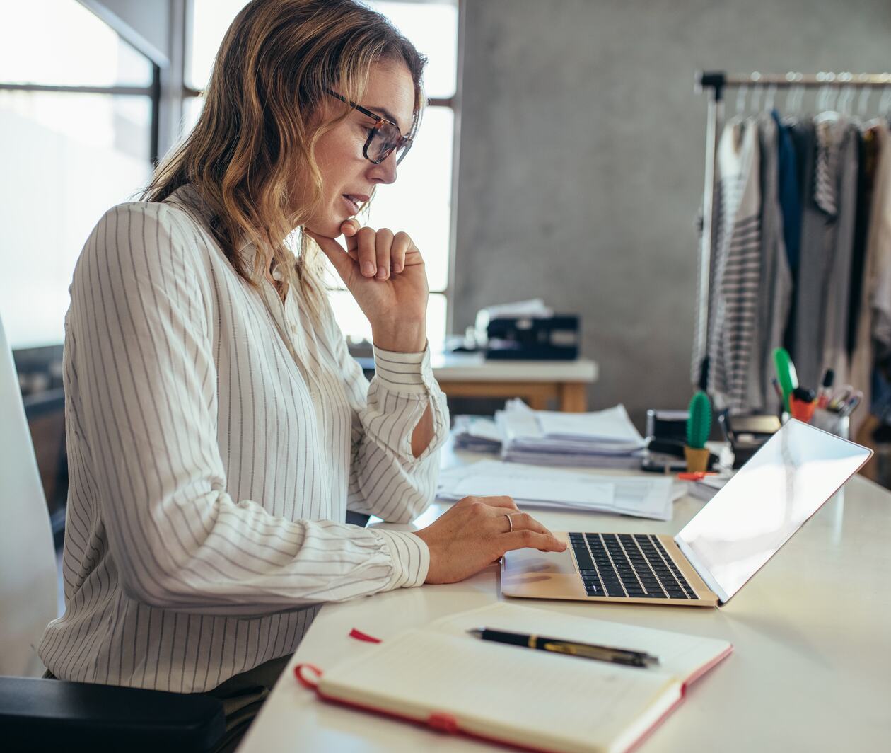 Woman in a office wear sat at her desk looking at her MacBook.