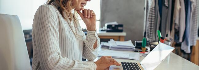 Woman in a office wear sat at her desk looking at her MacBook.