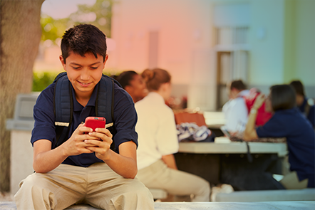 Niño de escuela usando su teléfono móvil afuera a la hora del almuerzo
