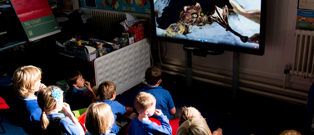 A group of primary school children gather to watch a film in their classroom.