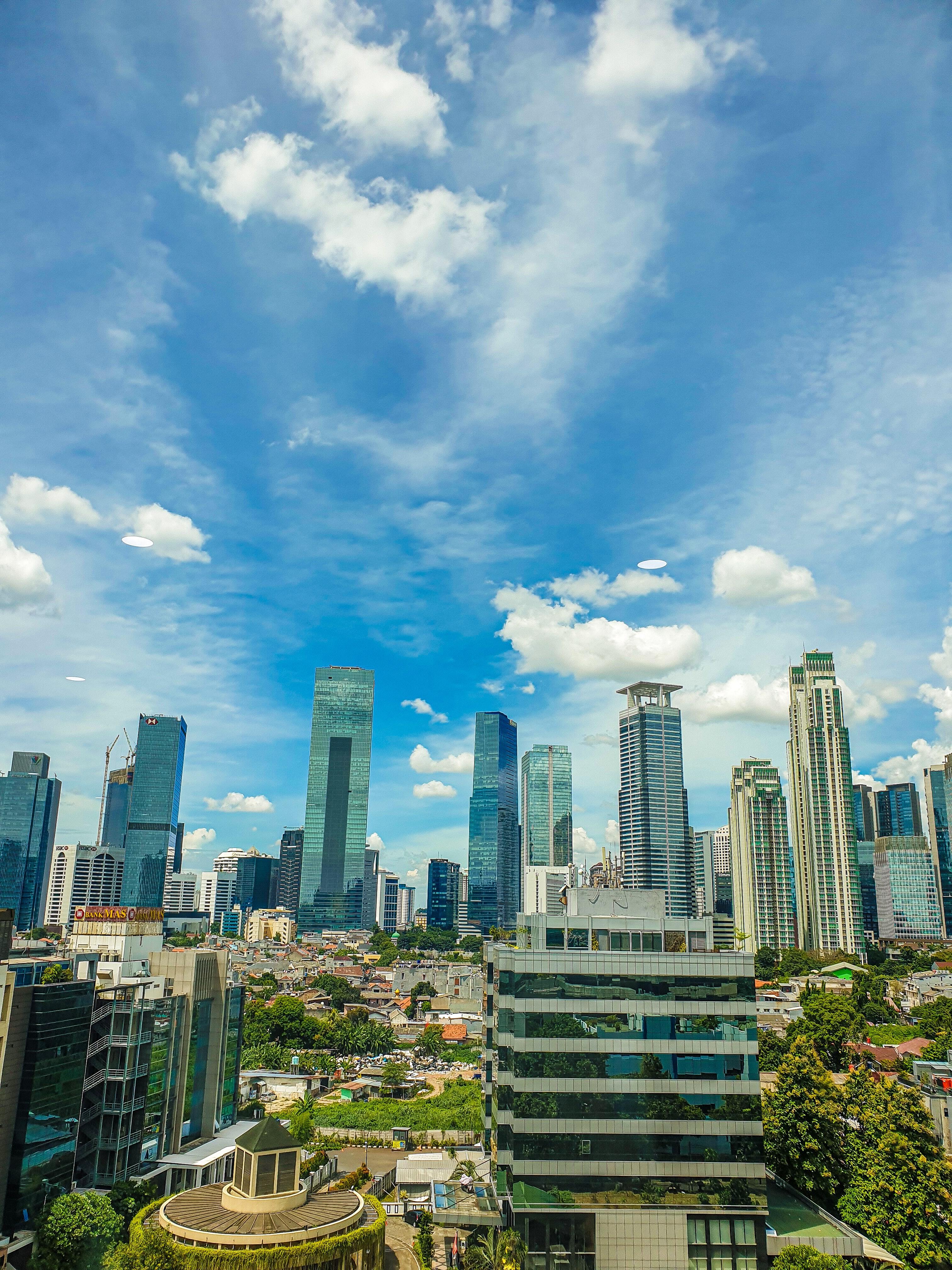 City skyline with a lot of trees between te buildings and a blue , cloudy but also sunny sky