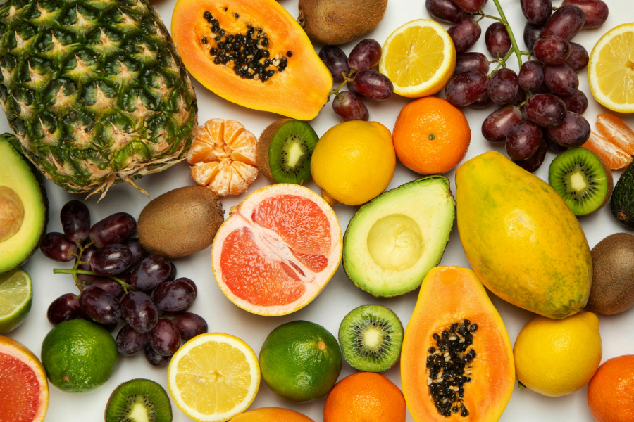 A selection of fruit A diverse assortment of sliced and whole fruits on a white background, including pineapple, papaya, kiwi, lemon, lime, grapes, avocado, grapefruit, and oranges.
