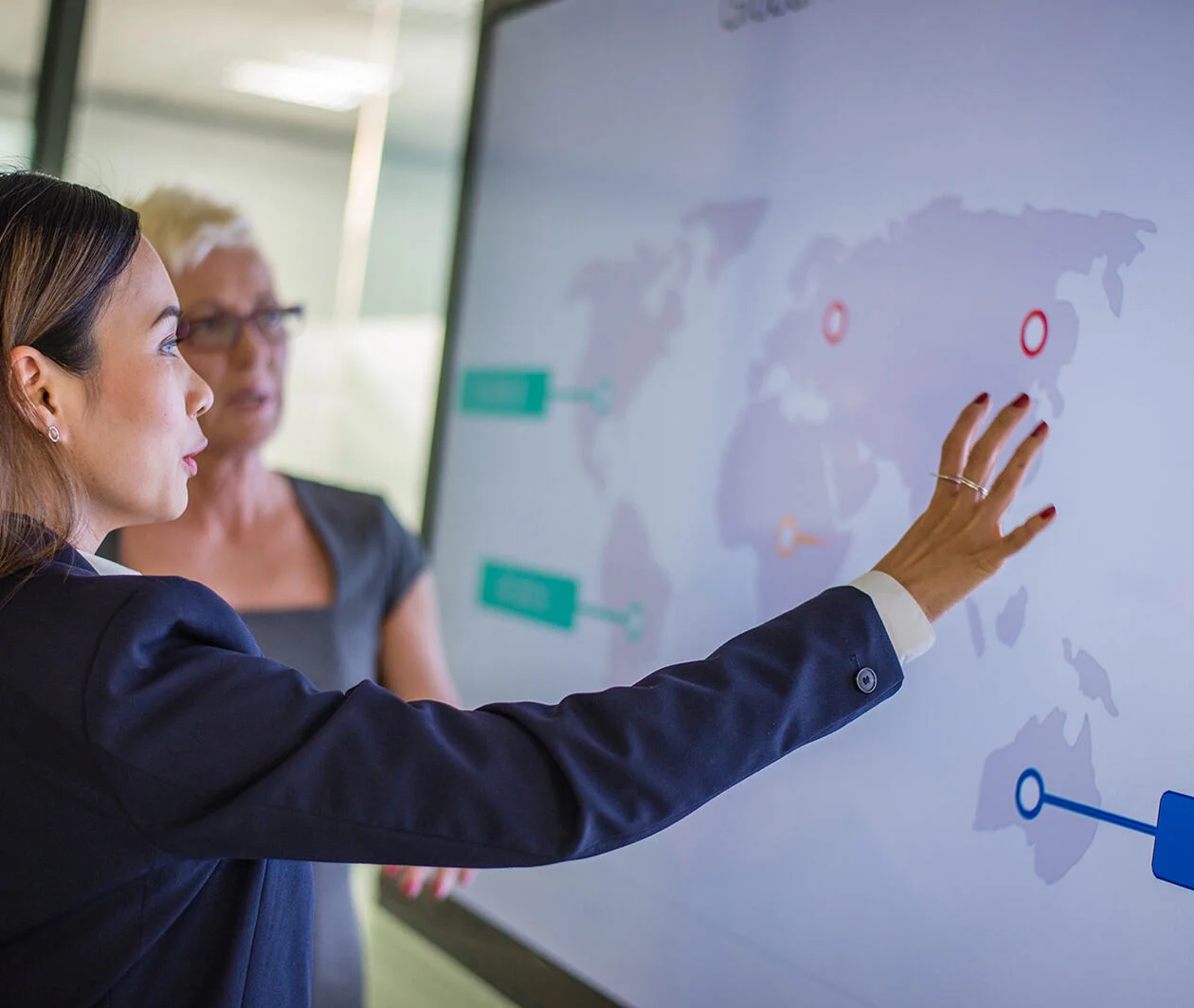 2 business women discussing on a world map within a big computer screen