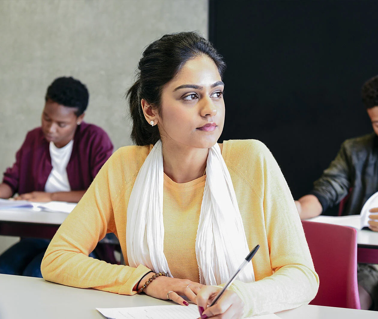 Young woman in university class, thinking and writing 