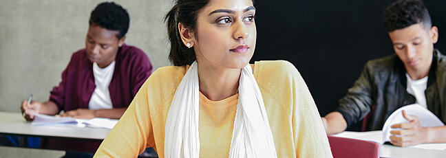 Young woman in university class, thinking and writing 