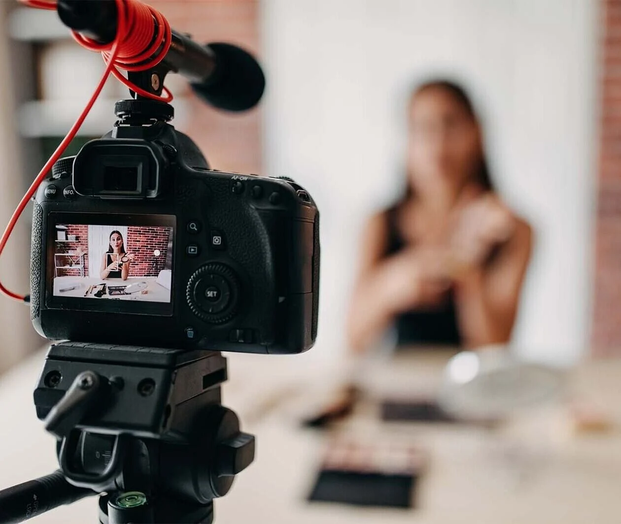 The blurry outline of a woman sitting down at a desk with a camera and microphone recording her.