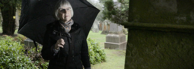 Genealogy: a lady looks at a tombstone in a graveyard while researching her family tree