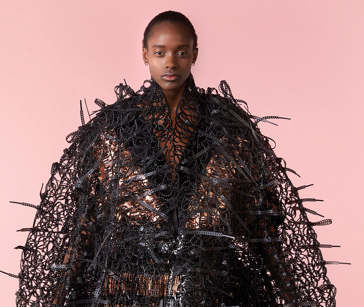 A model poses wearing an extravagant garment with a pink background.