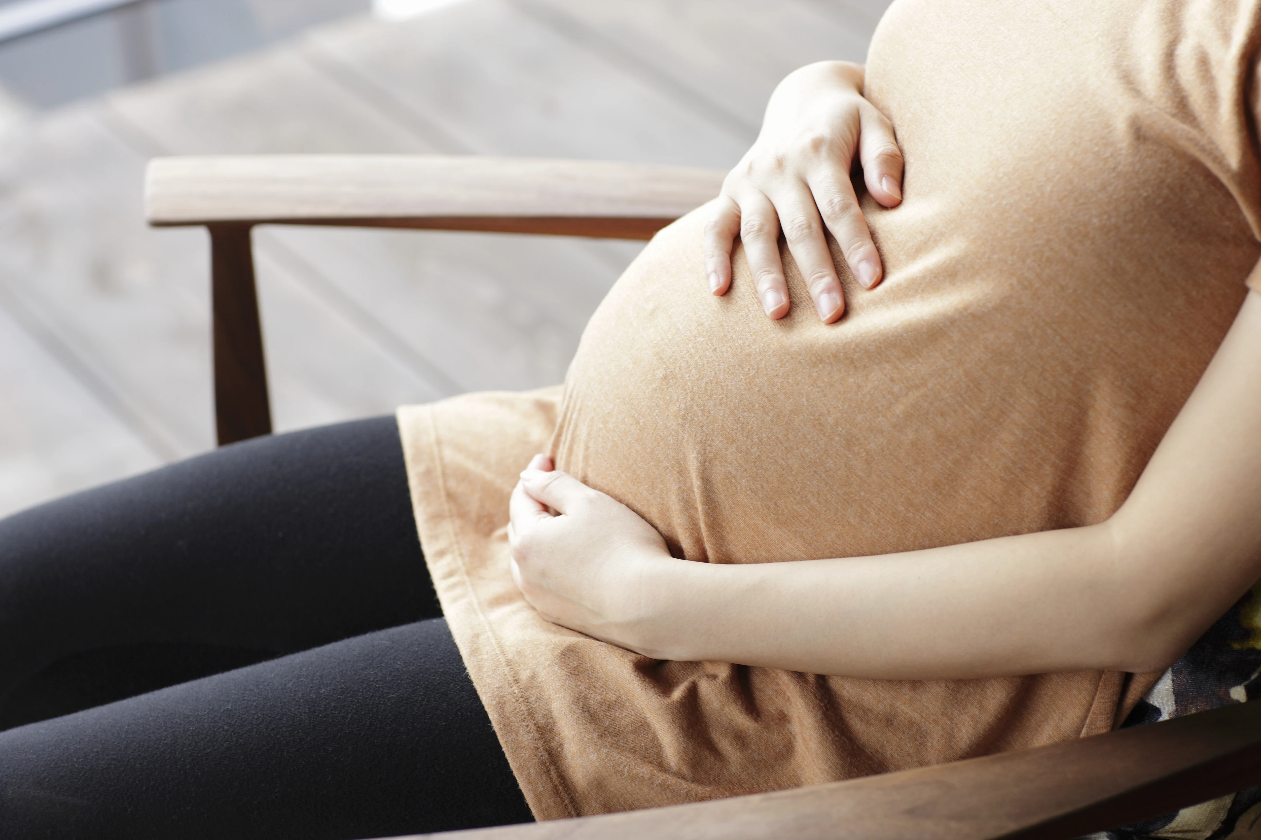 Pregnant woman touching abdomen sitting chair.