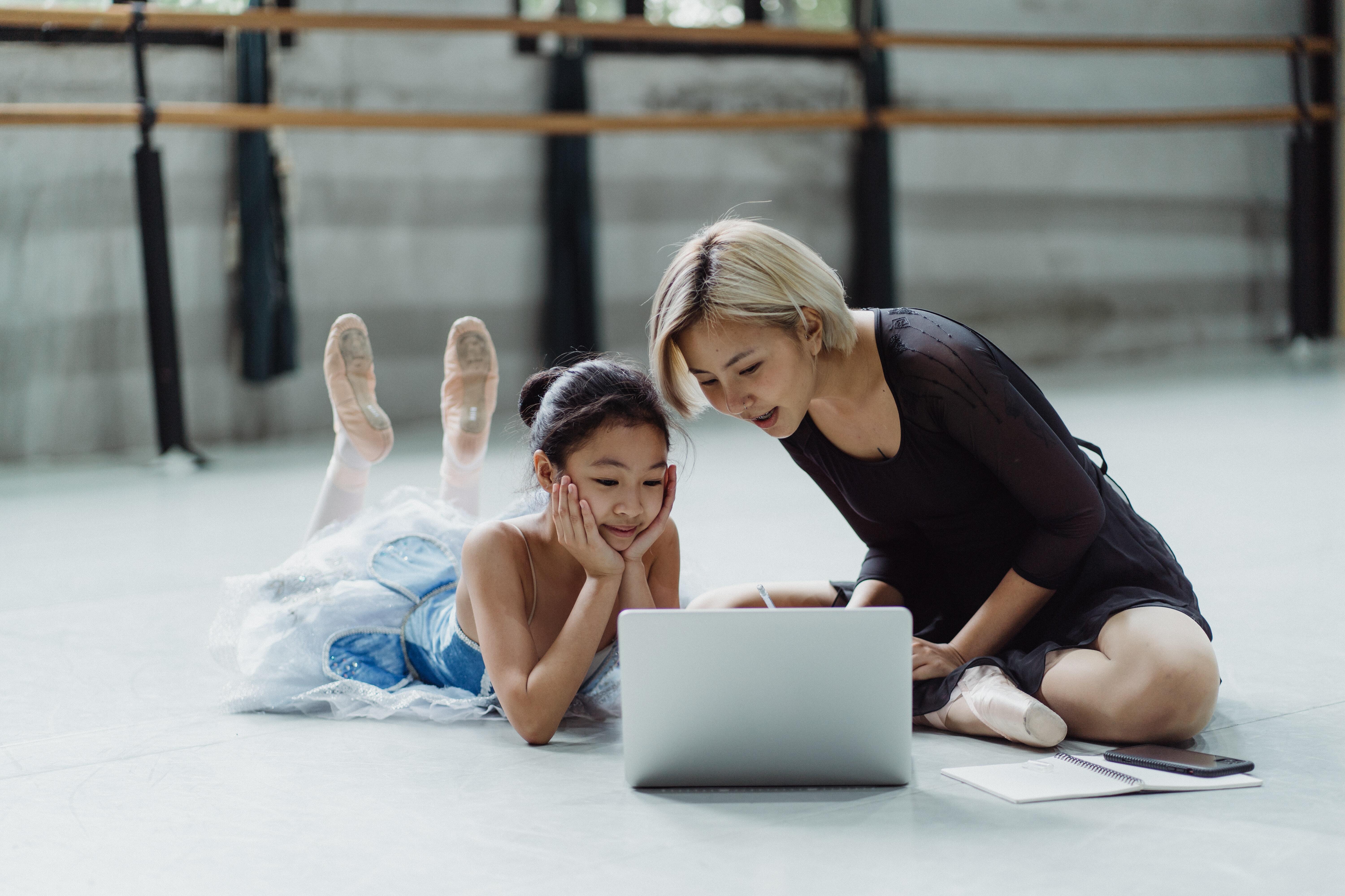 Supportive ballet teacher is sting down with student to show her how to properly do the tasks required