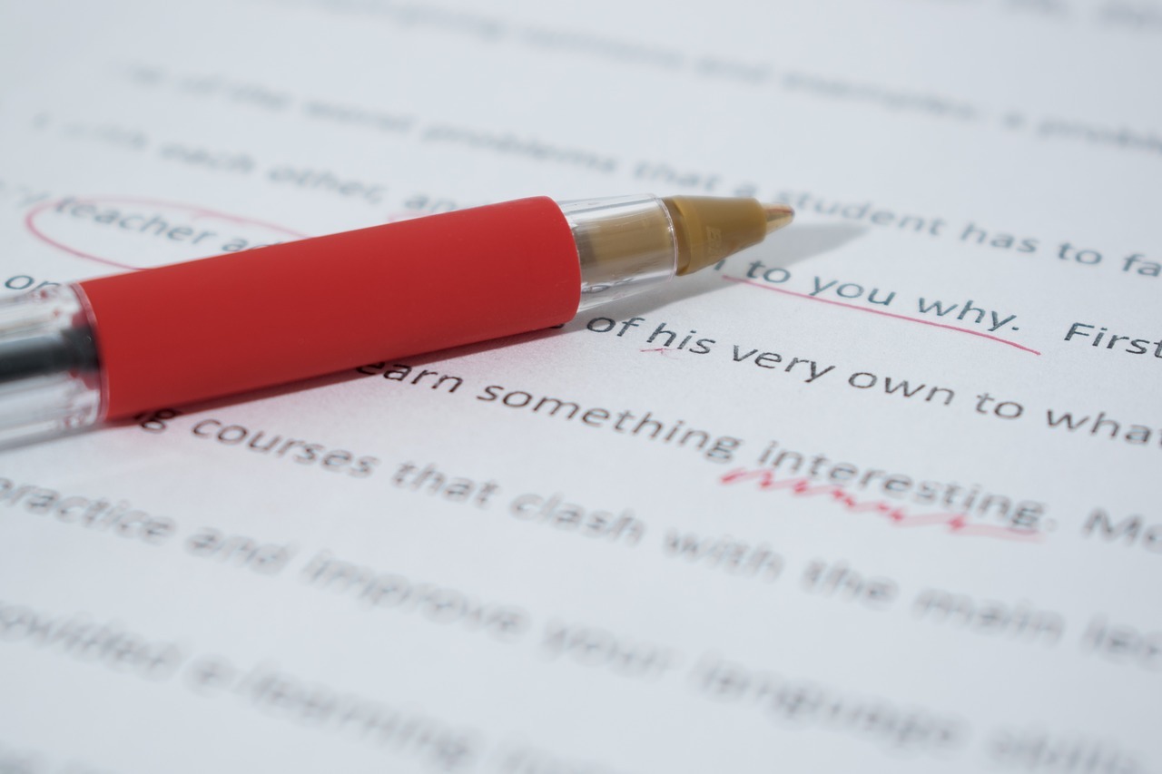 A red pen laid on a printed essay with corrections underlined and circled.