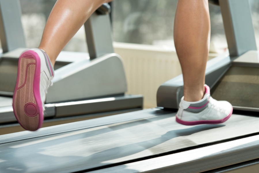 A person running on a treadmill with pink and white shoes.