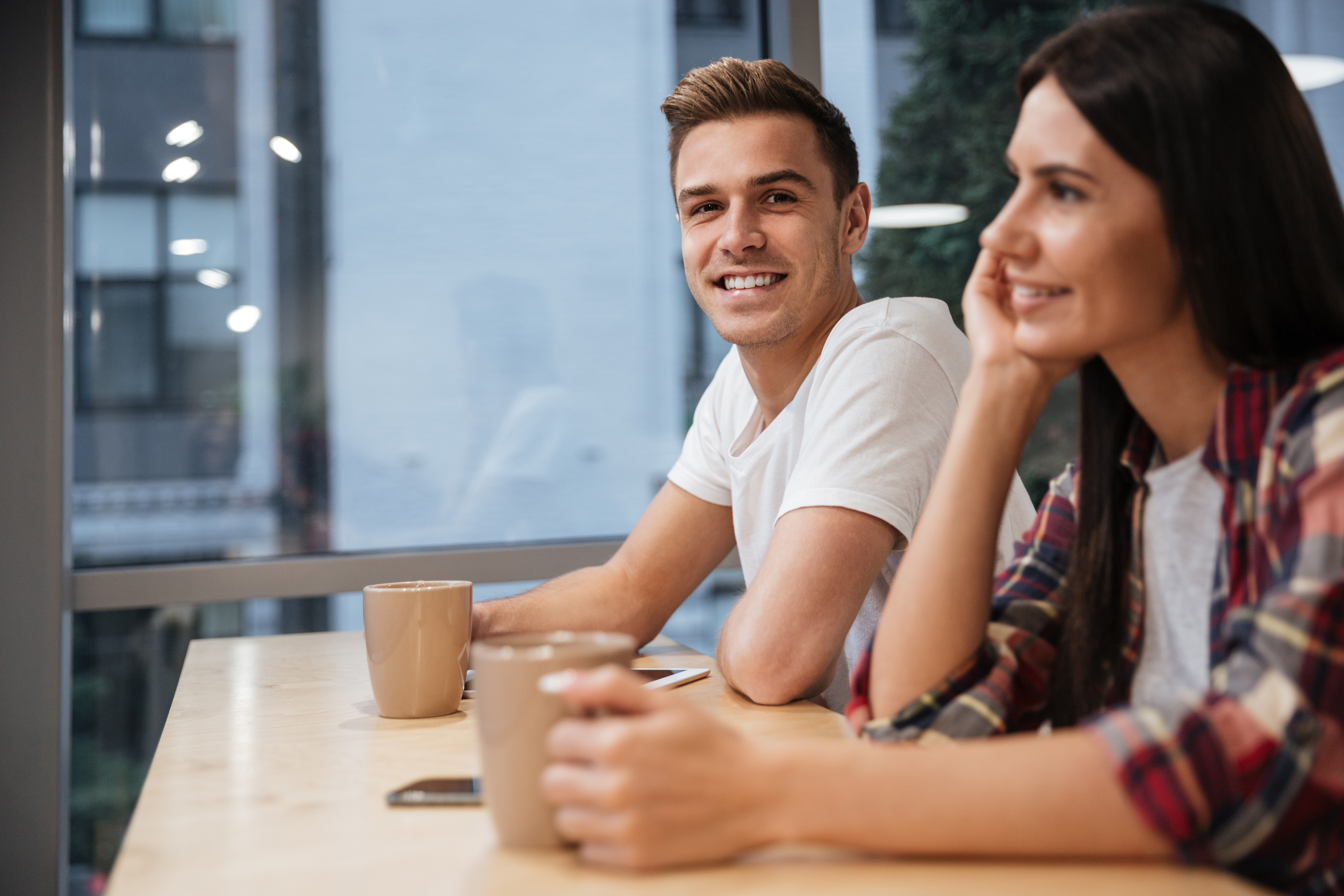 Side view of Coworkers sit by the table with coffee in office. Man looking at camera