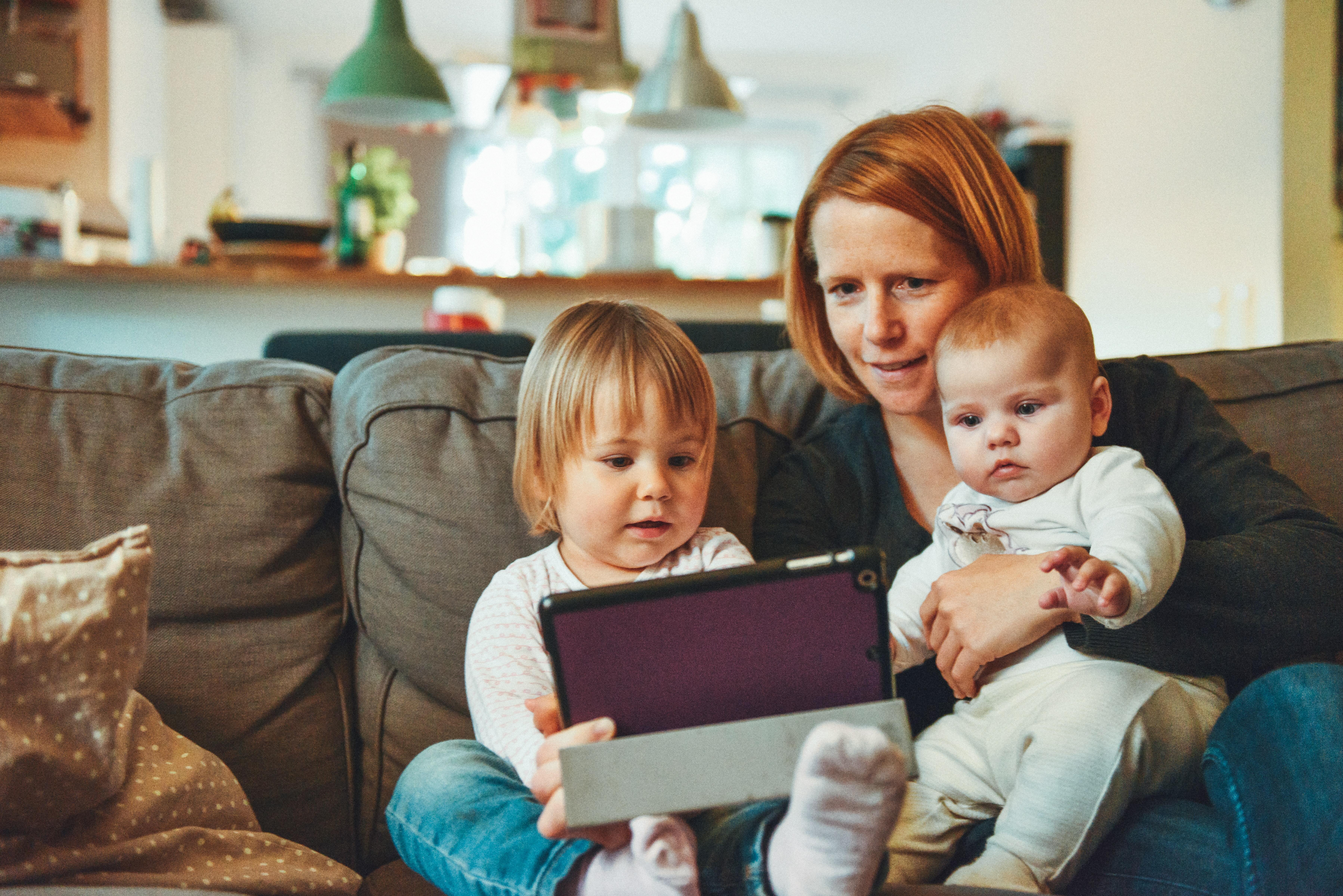 Mother sits on sofa with two young children on video call.