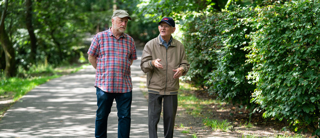 Two senior men walking down a ver leafy park