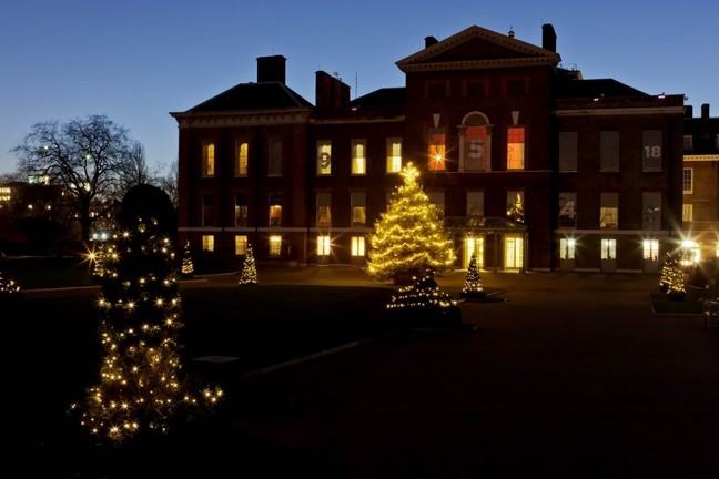 A landscape photograph of Kensington Palace at night, illuminated by trees with Christmas lights