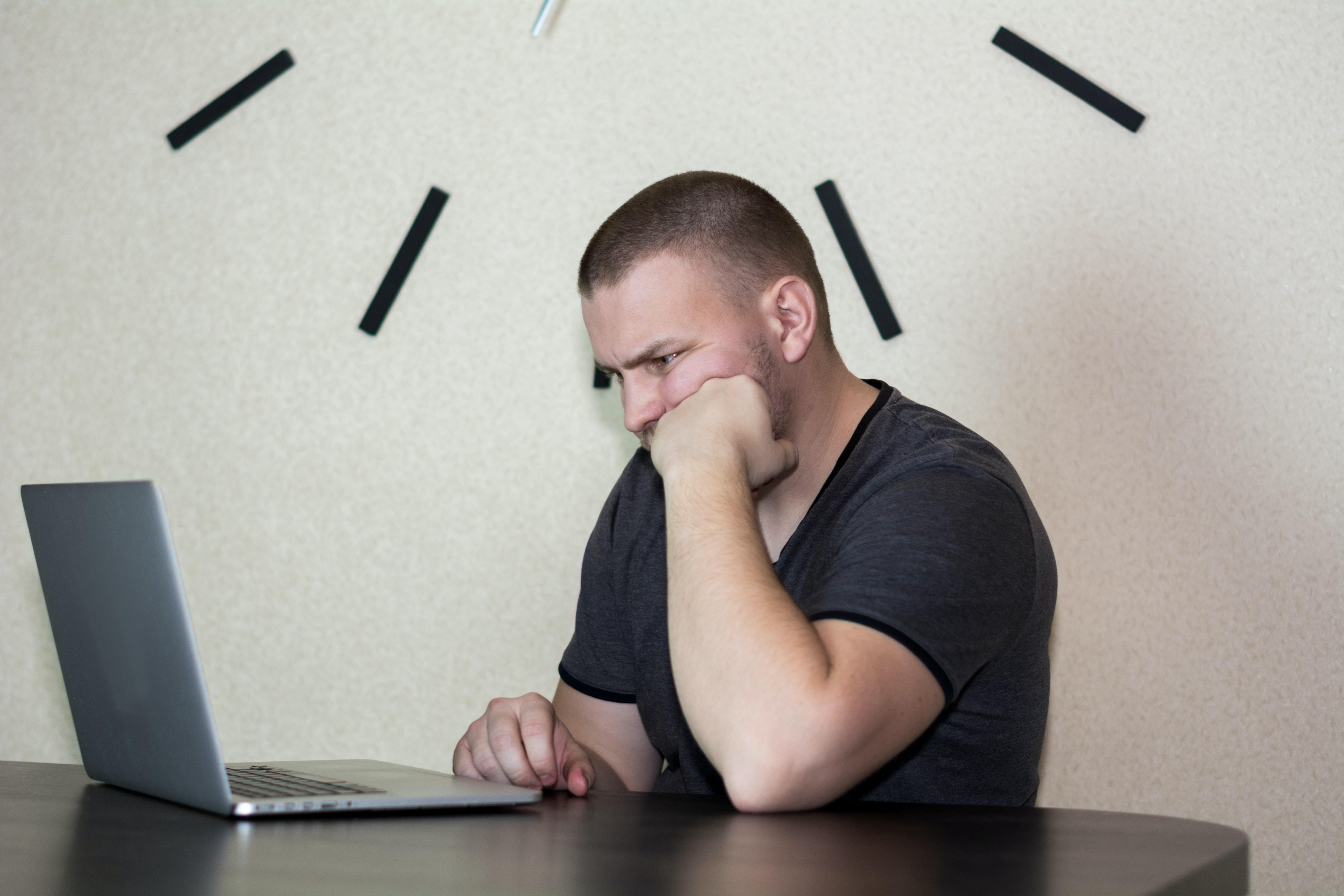 Man sitting at a table in front of a computer with his chin on his fist