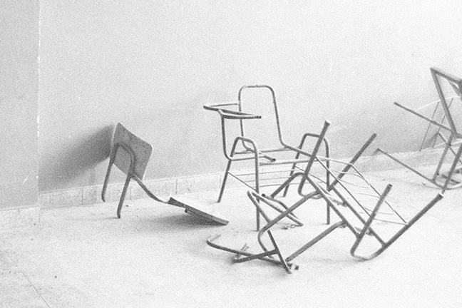Black and white image of broken desks in an abandoned classroom