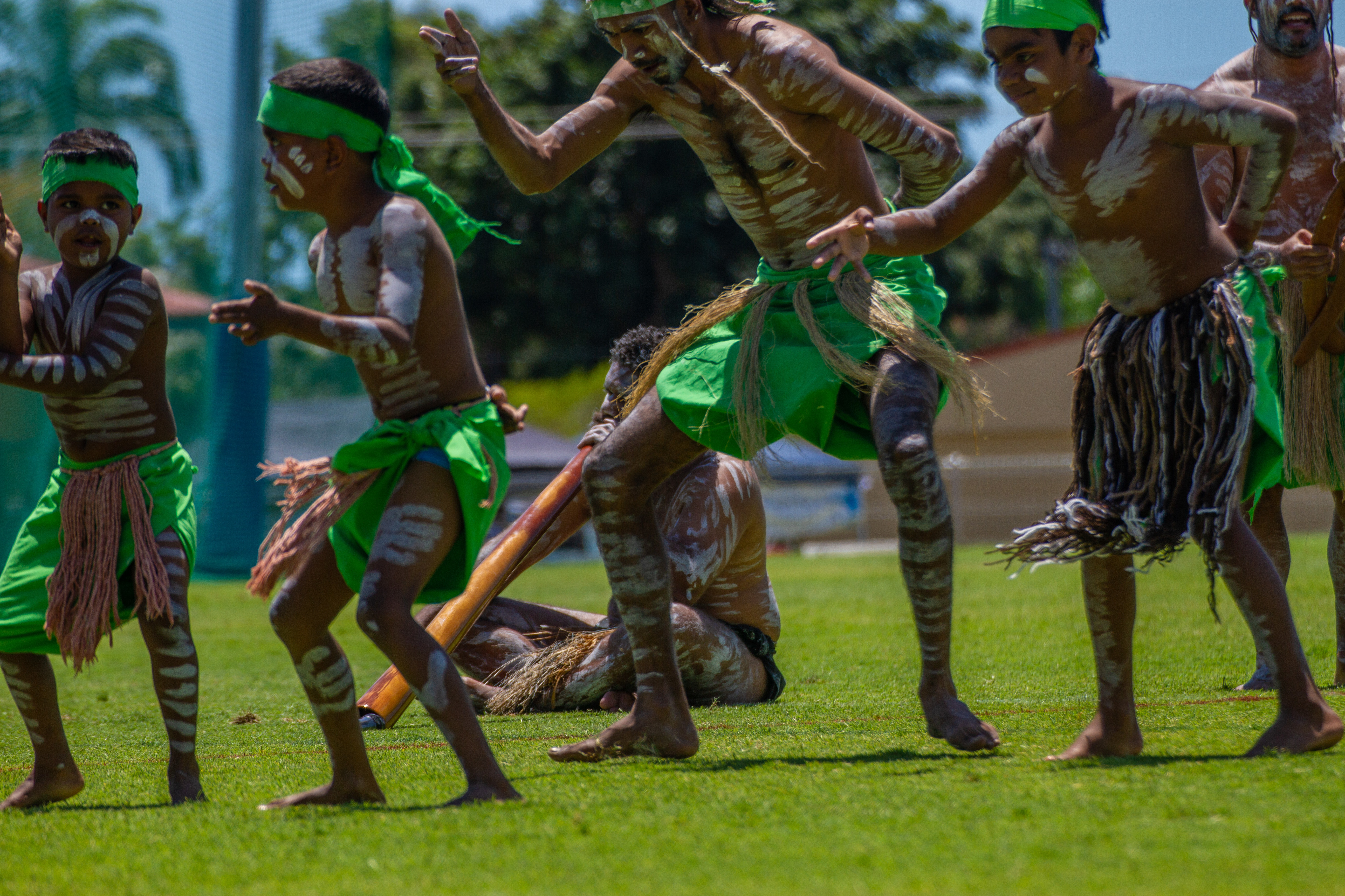 A group of young Aboriginal boys, dressed in traditional costume are dancing on the grass.