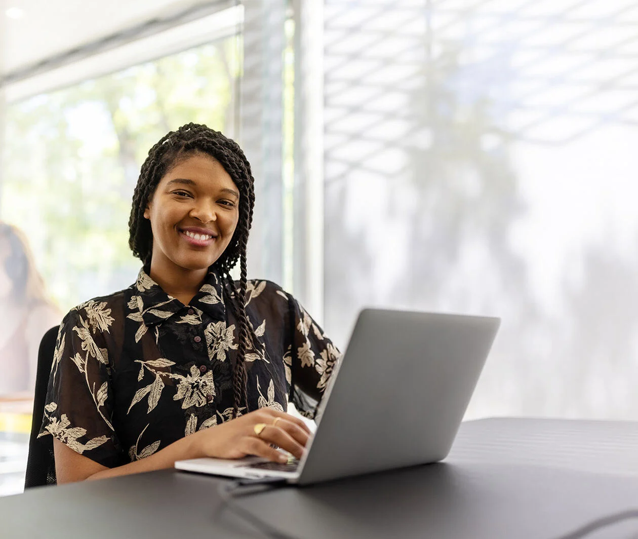 A woman smiles as she sits at a wooden desk with her laptop.