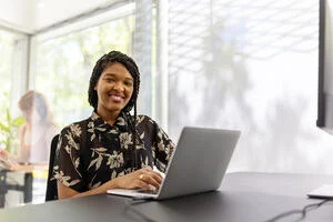 A woman smiles as she sits at a wooden desk with her laptop.