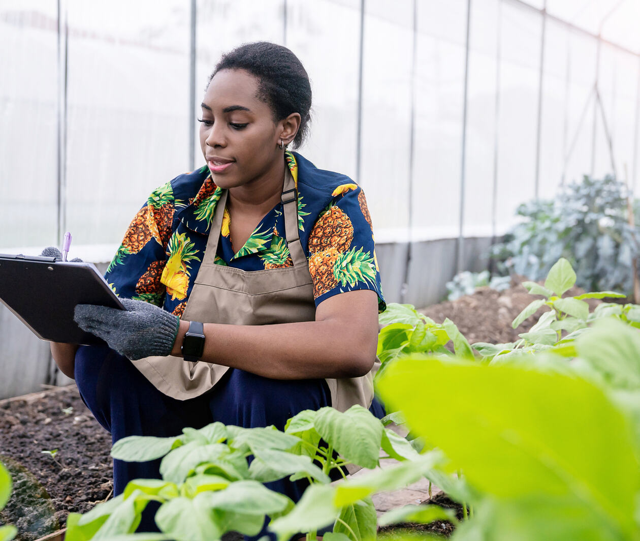 Woman smiling and writing on a clipboard in a greenhouse.