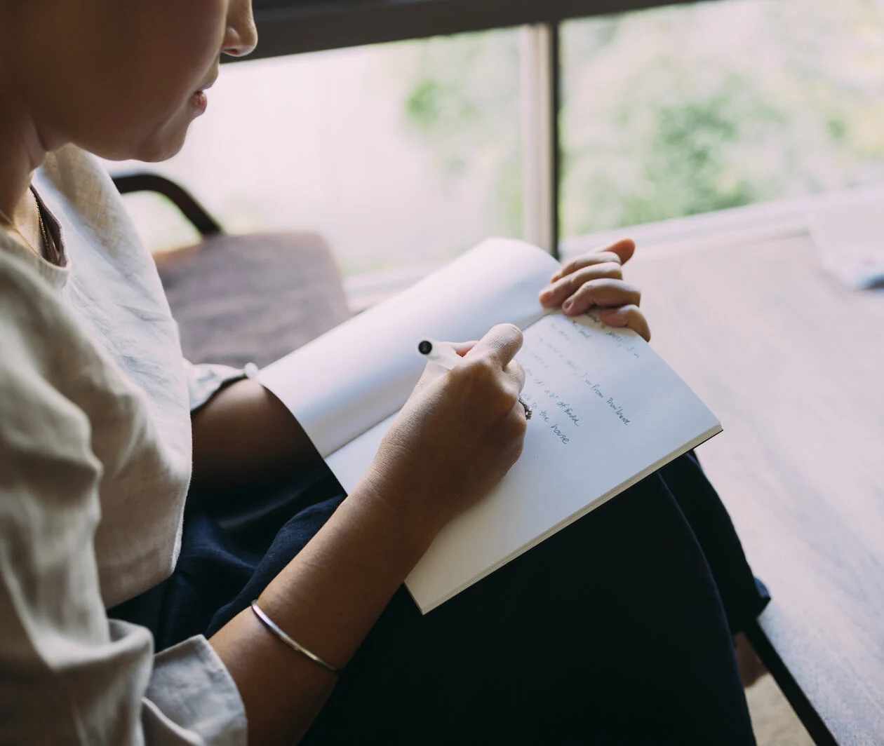 Person sitting down while writing in a book.