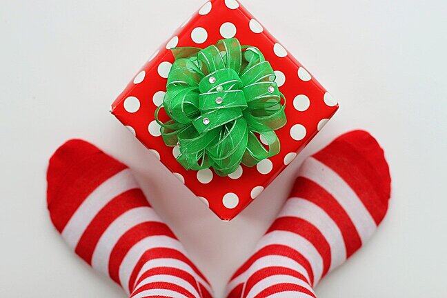 Feet in a pair of exactly matching striped socks framing a present in wrapping paper