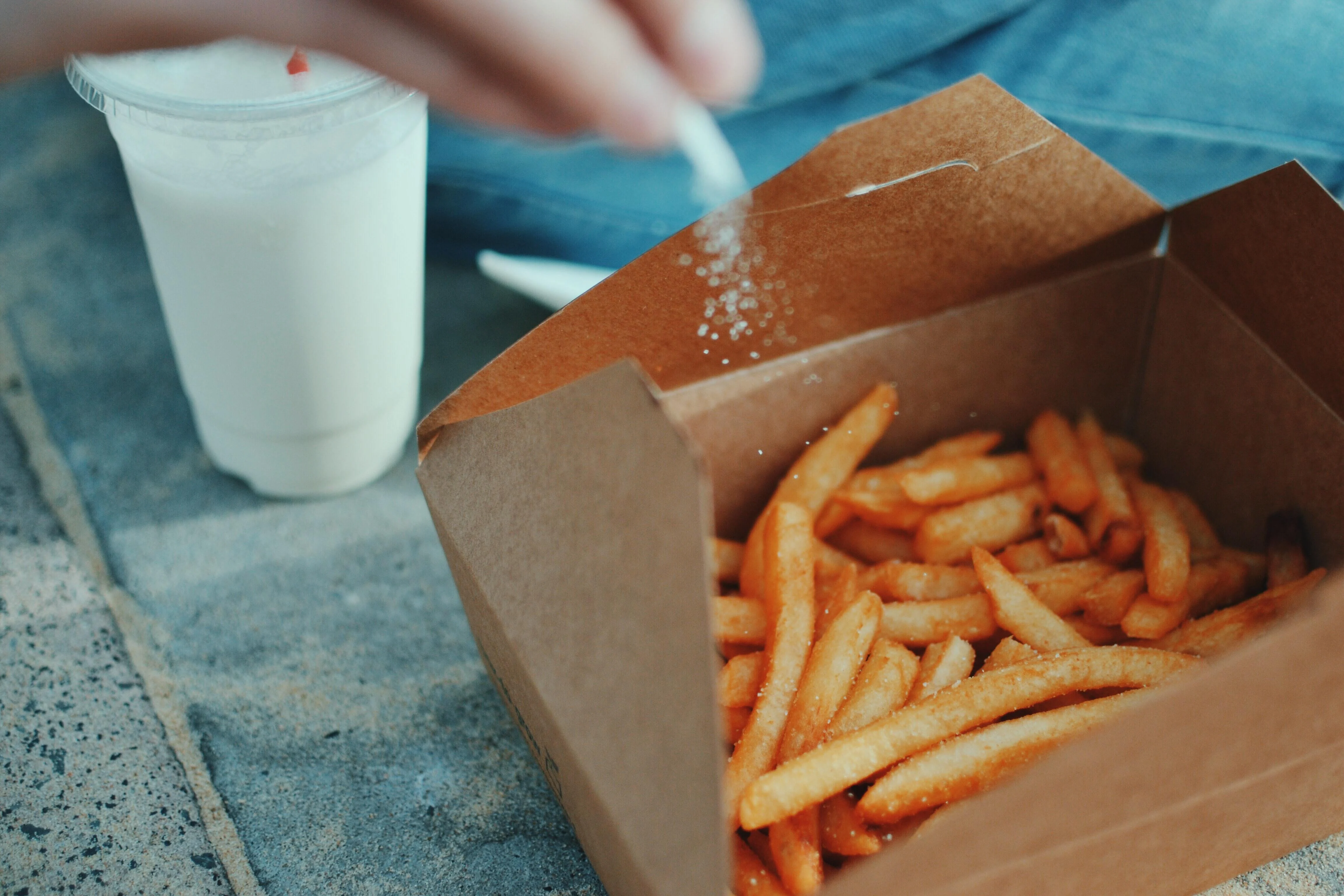 Person sprinkling salt on fries