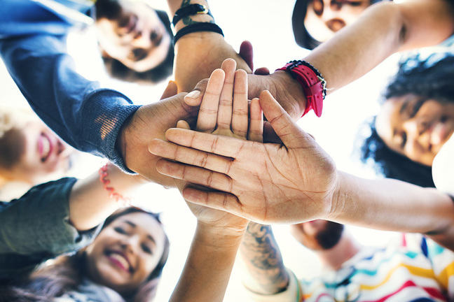 Happy people standing in a circle with their hands joined in the centre
