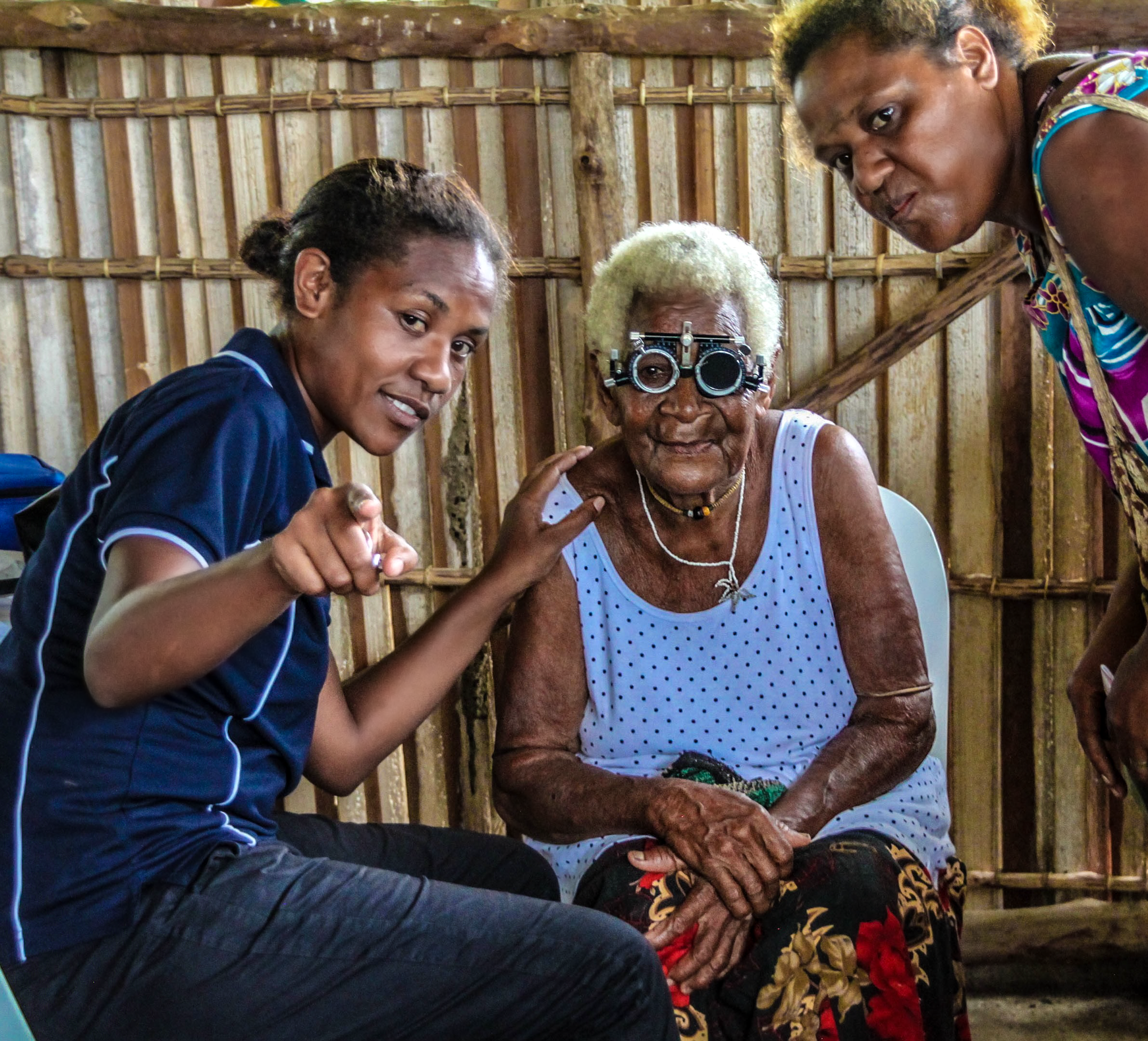 Edllderly femal patient wearing refraction spectacles accompanied by female carer and examined by female health worker