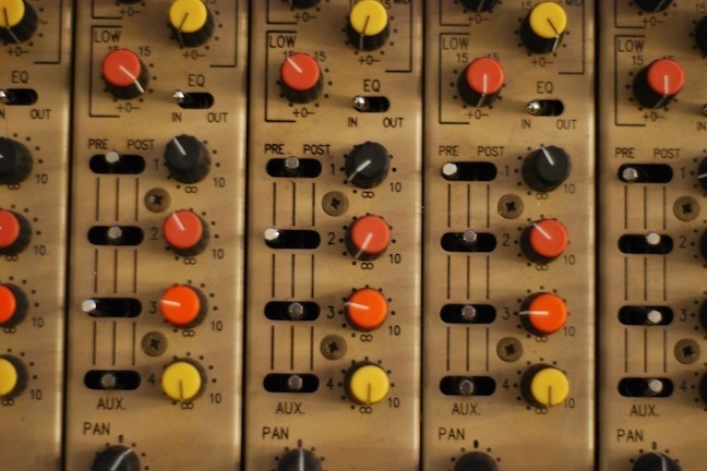 A sound mixing board with many different knobs in the colors yellow, orange and black.