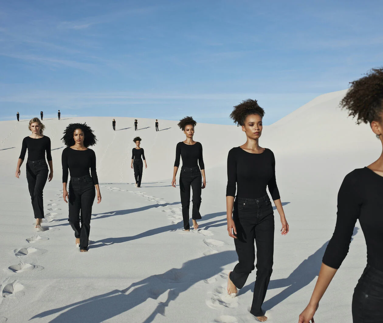 A group of women of different ethnicities walk through a desert landscape