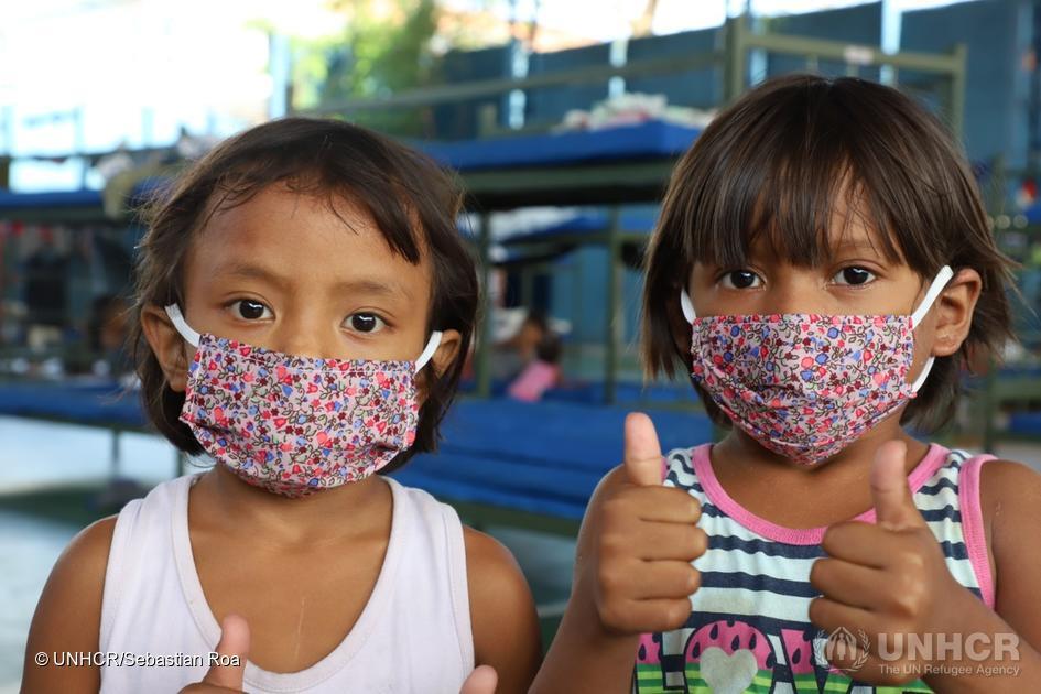 Two young girls wearing masks with their thumbs up